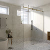 A close-up view of a satin brass sliding shower door system installed in a modern bathroom with patterned tile flooring.