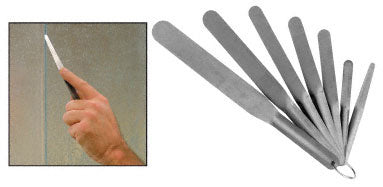 A hand uses a flat, flexible stainless steel spatula to apply sealant, alongside a full set of seven spatulas on a ring.