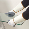 A person wears a pair of white polyester mesh wrist protectors while handling a sheet of glass.