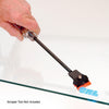 A hand uses a scraper tool equipped with an orange plastic blade to remove a decal from a glass surface.
