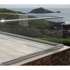 A glass balcony railing installed with a polished brass cap rail overlooking a coastal landscape.