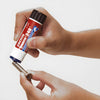 A hand applies Loctite 248 threadlocker from the stick onto the threads of a metal screw.