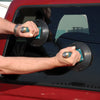 A person uses two CRL Wood's Powr-Grip vacuum cups to lift a glass window panel on a vehicle.