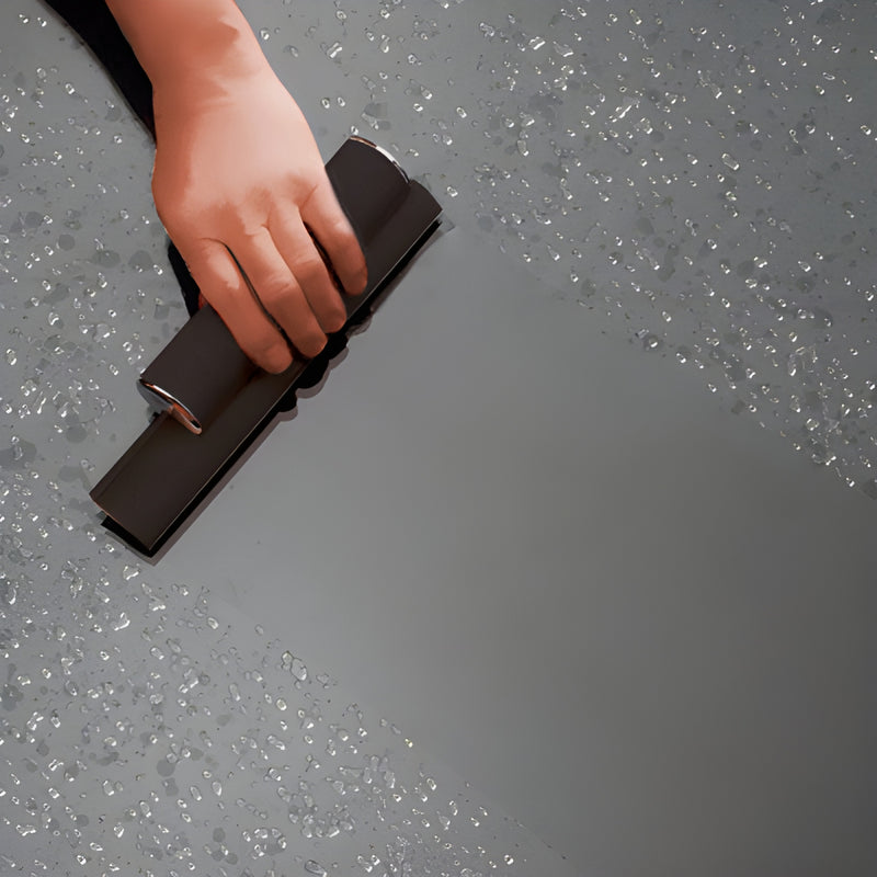 Hand-held black dual-blade squeegee with chrome end caps wiping water from a glass surface.